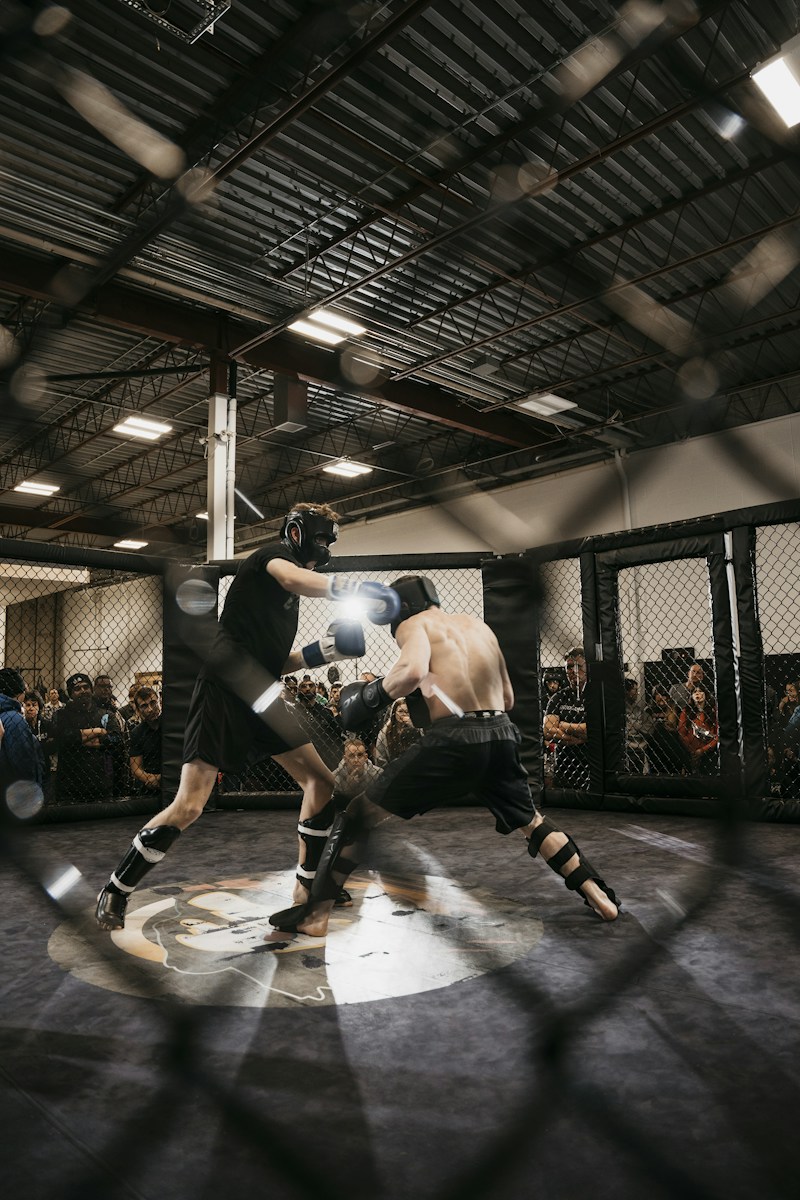 Two athletes sparring with protective gear in an MMA cage.